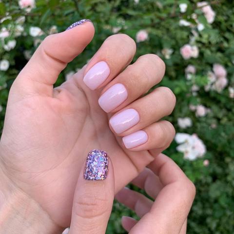 Light mauve manicure in natural light, hand posed near garden flowers